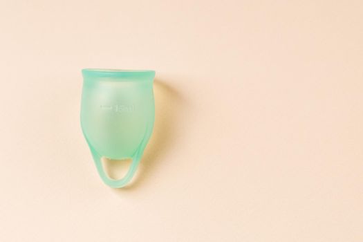 Blue silicone menstrual cup on beige pastel background with copy space