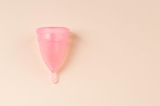 Pink Menstrual cup on bright beige background. Alternative eco friendly feminine hygiene product. Copy space.