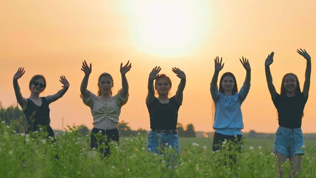 Girls friends waving their hands to the setting sun on the background of the sunset