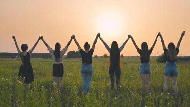 Girls friends raise their hands at sunset