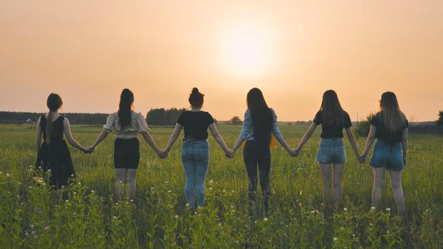 Girls stand holding hands at sunset on a summer evening
