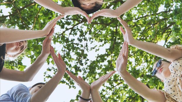 A group of girls makes a heart shape from their hands against the background of tree branches