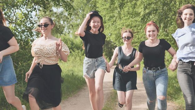 A group of girls run along the village road by the forest holding hands