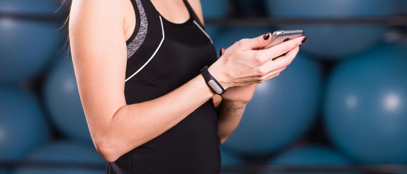 Close up of woman using cell phone and fitness tracker in gym.