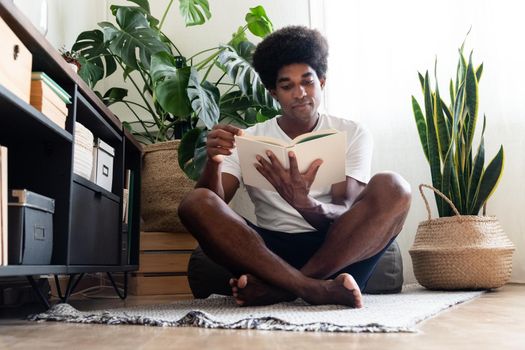 Young african american man reading peacefully in his cozy, bright apartment. At home concept.