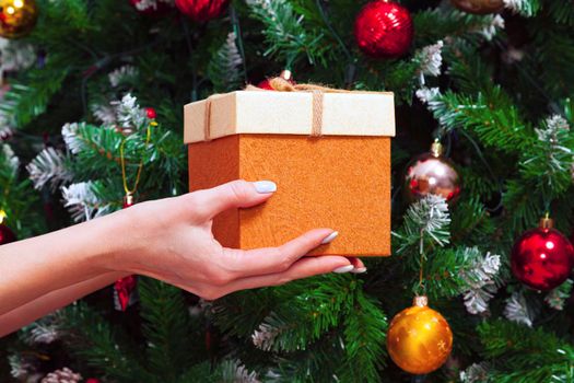 Female hands holding a gift box against decorated Christmas tree