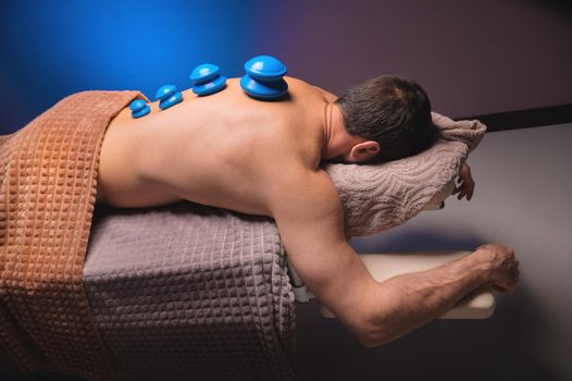 Vacuum rubber cups for cupping therapy on the back of a naked man. Massage at the spa, getting medical treatment for the back. Revitalizing and relaxing massage, fitness treatments.