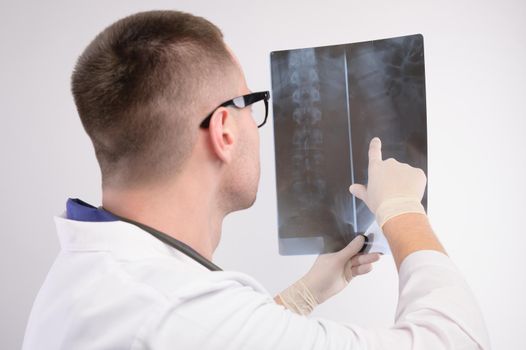 Young caucasian doctor a radiologist is looking at an x-ray. A doctor in a white coat with glasses with a stethoscope holds an x-ray in his hand.