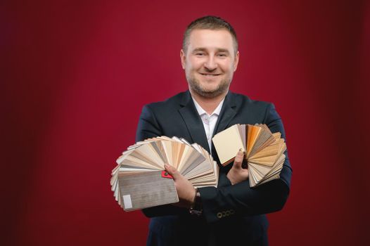 Confident business leader or manager standing in the studio with samples of furniture coverings, smiling at the camera. Caucasian businessman owner of his own furniture business.