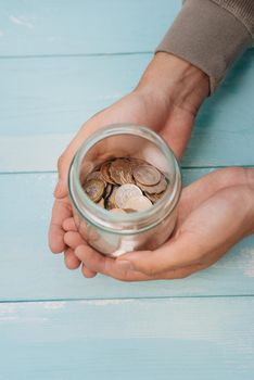 Young man hands holding glass jar with money (coins) inside