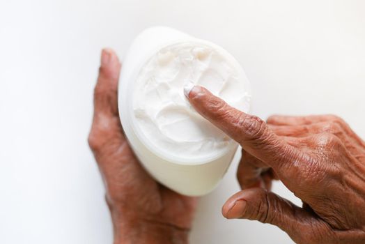 senior woman applying beauty cream onto skin .