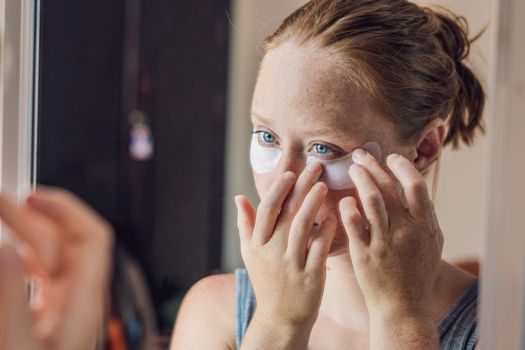 Portrait of Beauty Red-haired woman with eye patches showing an effect of perfect skin. Spa Girl.