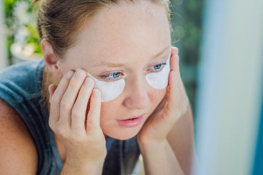 Portrait of Beauty Red-haired woman with eye patches showing an effect of perfect skin. Spa Girl.