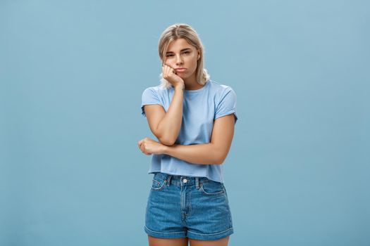 Lifestyle. Studio shot of displeased moody girlfriend feeling disappointed boyfriend spoilt date leaning head on palm sulking from dissatisfaction and squinting being offended posing over blue background.