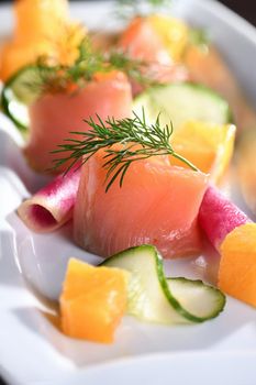 Buffet serving of pickled salmon slices with radish, cucumber and orange cubes