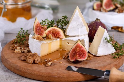 Brie cheese served on a wooden board with figs, walnuts and honey
