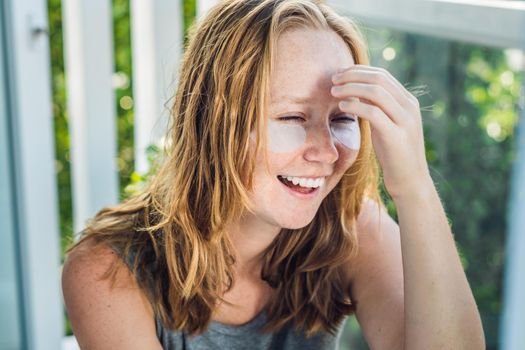 Portrait of Beauty Red-haired woman with eye patches showing an effect of perfect skin. Spa Girl.