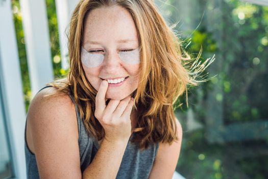 Portrait of Beauty Red-haired woman with eye patches showing an effect of perfect skin. Spa Girl.