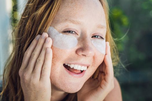 Portrait of Beauty Red-haired woman with eye patches showing an effect of perfect skin. Spa Girl.