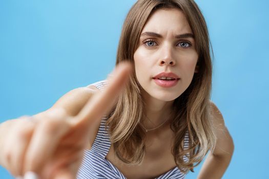 Curious and intrigued woman poking at camera with finger as if checking anyone there looking at her, bending forward with serious interested expression frowning, pressing forefinger to lense.