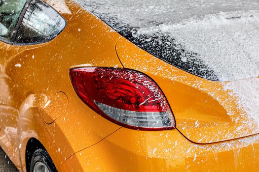 Yellow car rear window completely covered with thick white shampoo foam, when washed in carwash.