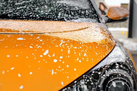 Yellow car front covered with shampoo foam, when washed in carwash.