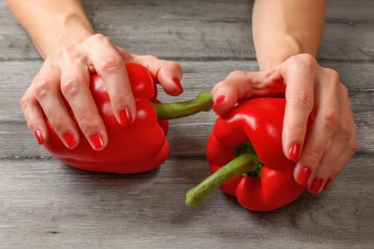 Woman hands holding two red bell peppers placed on gray wood desk.