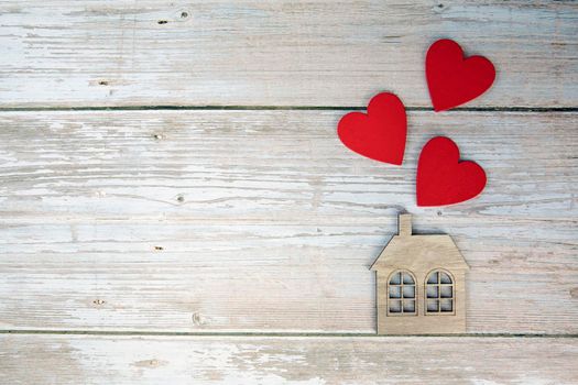 Wooden house with three red hearts on a wooden background. Love nest, love relationships. Buying a house with a young family. Affordable housing. banner. Family psychology, strong relations. copy space top view background space for text