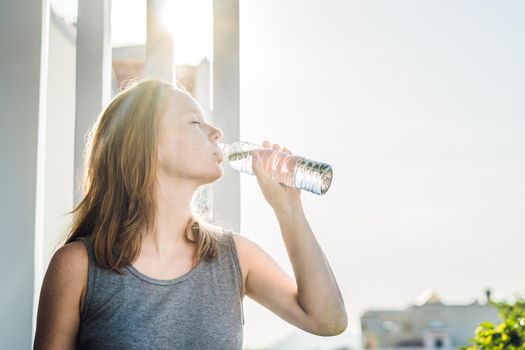 Young woman is drinking water on the sunset background.