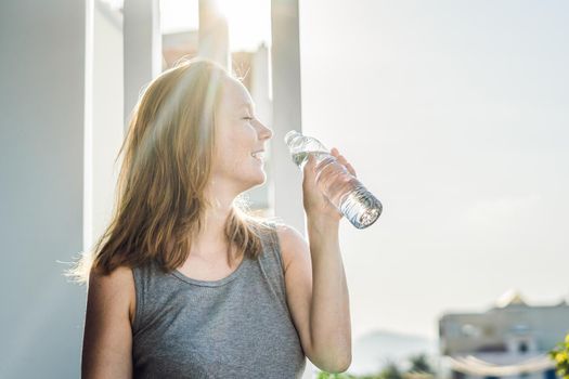 Young woman is drinking water on the sunset background.