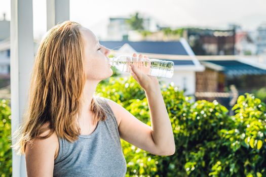 Young woman is drinking water on the sunset background.