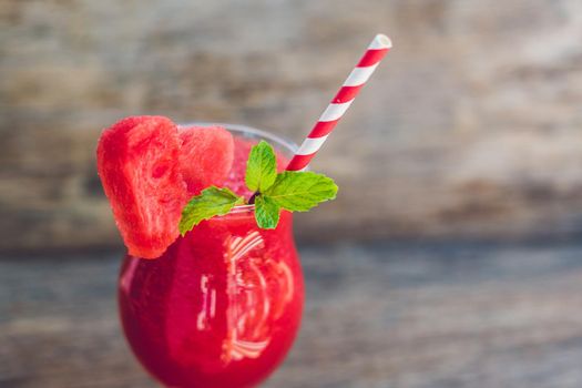 Healthy watermelon smoothie with mint and striped straws on a wood background.