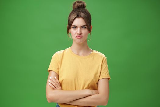 Girl not liking result of work looking displeased and serious at camera, frowning crossing hands against chest, pursing lips from disappointment, being offended over green background.