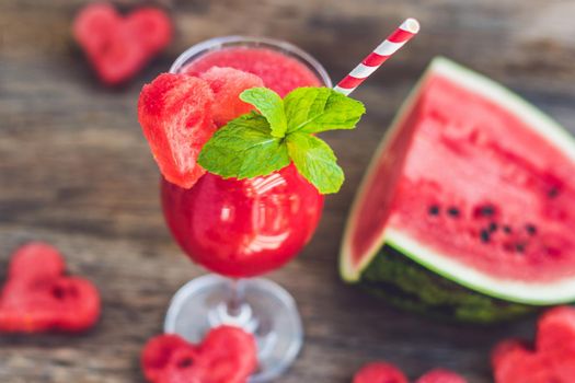Healthy watermelon smoothie with mint, a piece of watermelon, hearts and a striped straw on a wood background.