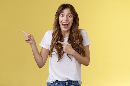 Happy sincere cheerful young surprised woman see celebrity lose speech stare excited unbelievable awesome luck fascinated pointing index fingers left open mouth stunned thrilled yellow background. Lifestyle.