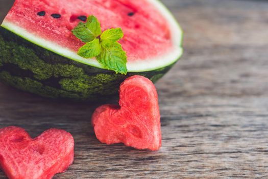 Healthy watermelon smoothie with mint, a piece of watermelon, hearts and a striped straw on a wood background.