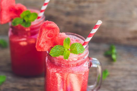 Healthy watermelon smoothie in Mason jars with mint and striped straws on a wood background.