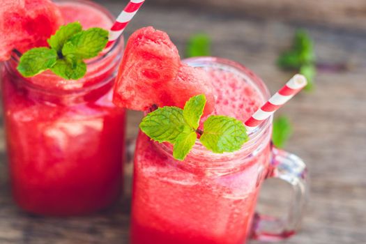 Healthy watermelon smoothie in Mason jars with mint and striped straws on a wood background.