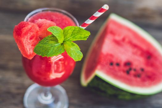 Healthy watermelon smoothie with mint, a piece of watermelon, hearts and a striped straw on a wood background.