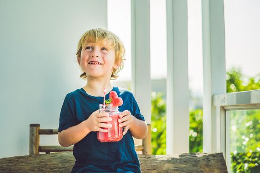 The boy is holding Healthy watermelon smoothie in Mason jar with mint and striped straws on a wood background.