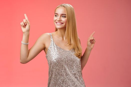 Carefree good-looking stylish glamour blond young 20s woman in silver glittering dress dancing having fun amused go wild party night prom shaking body raising index fingers up, red background.