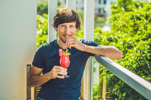 Man is holding Healthy watermelon smoothie with mint and striped straws on a wood background.