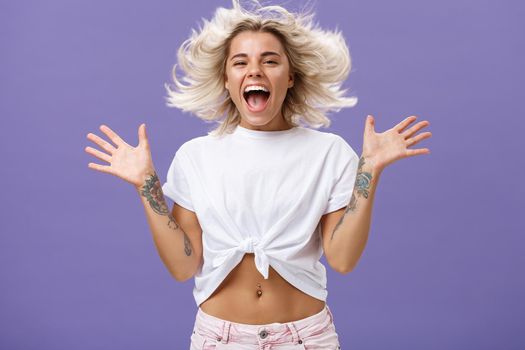 Lifestyle. Studio shot of happy carefree and pleased joyful woman with blonde hair spreading palms aside in delighted pose smiling broadly and gazing entertained at camera jumping while having fun.