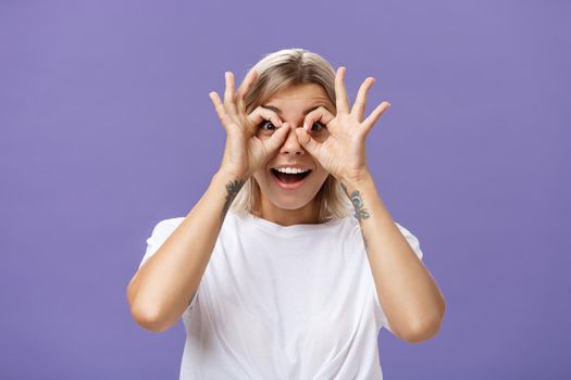 Looking at awesome discounts. Portrait of impressed amused and happy good-looking stylish young woman with tattoos on arms making circles with hands over eyes smiling with admiration at camera. Body language and advertising concept