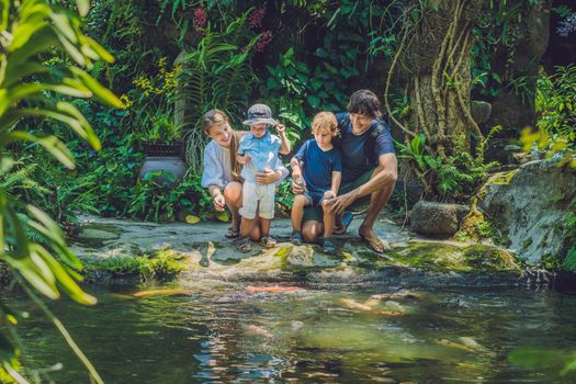 happy family feeding colorful Catfish in tropical pond.