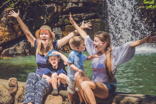 Tourists women and children against the waterfall with their hands raised.