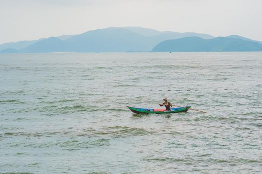 Vietnamese fisherman swims in a boat over the raging sea.