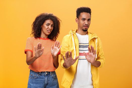 Two african american stylish friends hanging around interrupted by weird guy offering strange proposal shaking hands near chest in refusal and rejection gesture grimacing from aversion and dislike. People and emotions concept