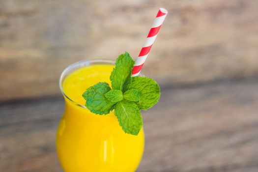 Juicy smoothie from mango in glass with striped red straw and with a mint leaf on old wooden background. Healthy life concept, copy space.