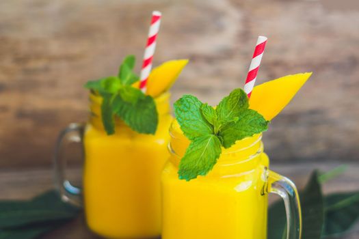 Juicy smoothie from mango in two glass mason jars with striped red straw on old wooden background. Healthy life concept, copy space.